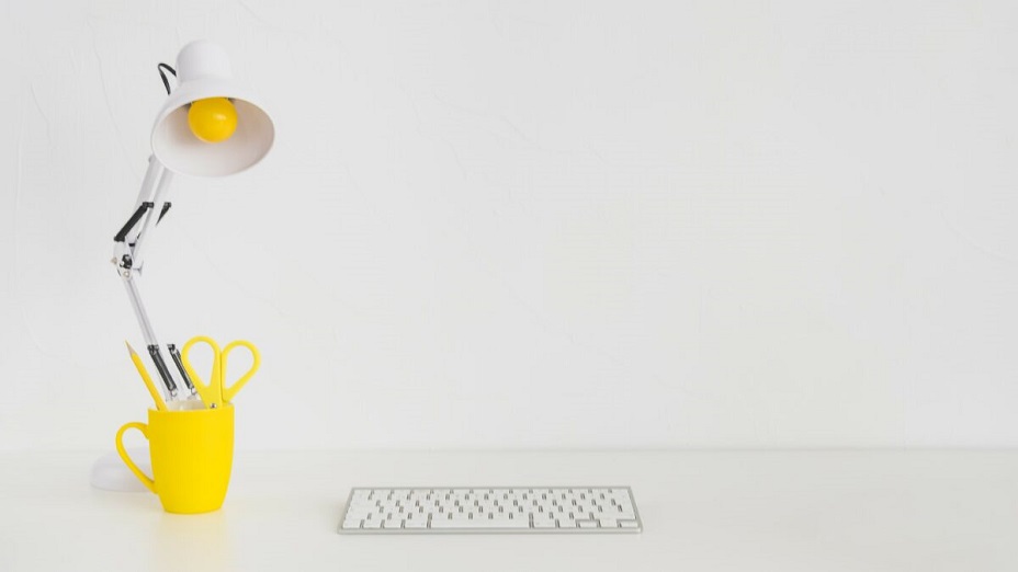 biurko z klawiaturą, żółtym kubkiem i lampką